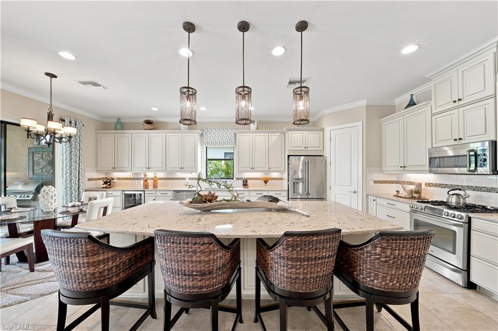 Spacious kitchen featuring an oversized island with a light-toned countertop, white cabinetry with crown molding, stainless steel appliances, and pendant lighting