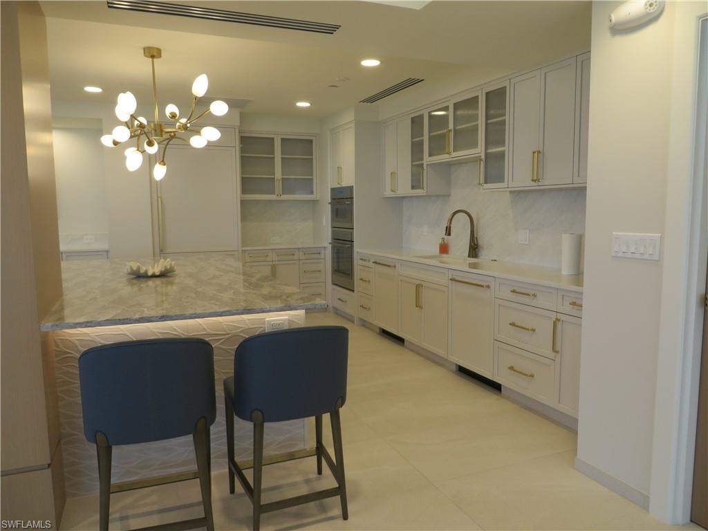 Social Room kitchen featuring backsplash, glass insert cabinets, recessed lighting, decorative light fixtures, and a kitchen breakfast bar