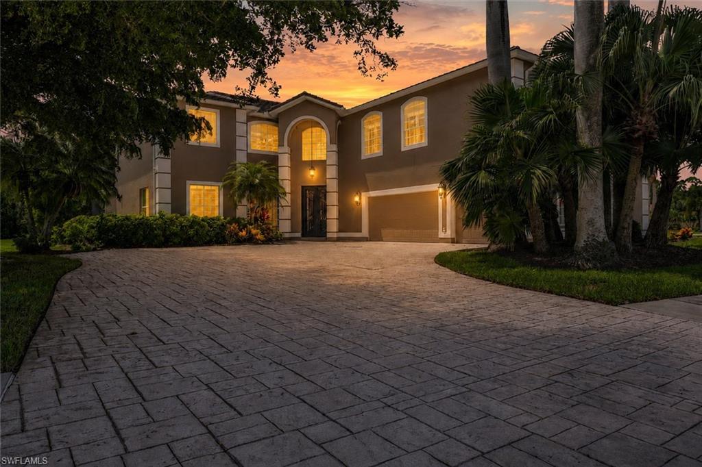 Stucco exterior with architectural details, arched entry, two-car garage, mature landscaping, and a paver driveway