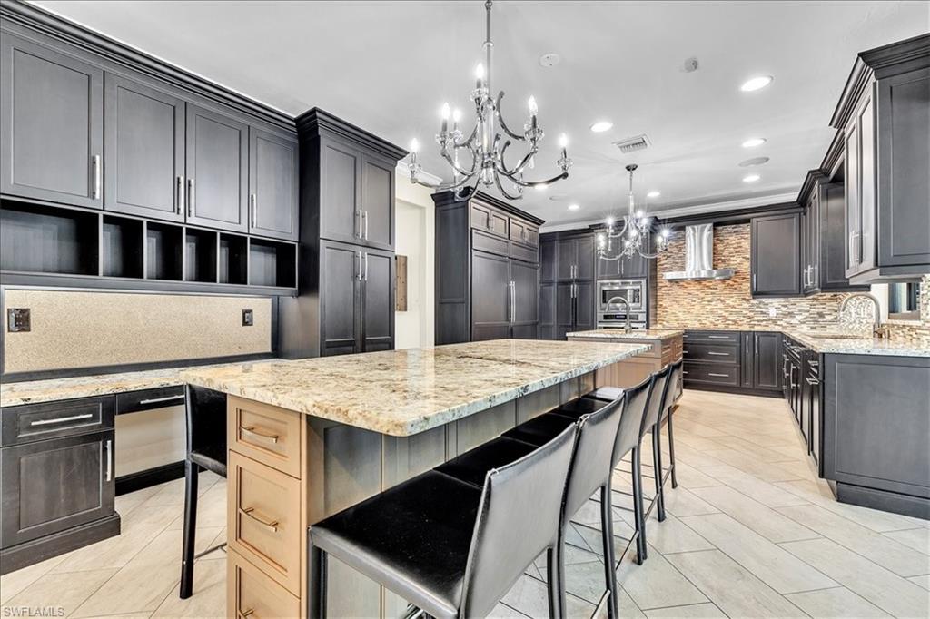Expansive kitchen featuring granite countertops, dark-finish cabinetry, tile flooring, and two chandelier light fixtures