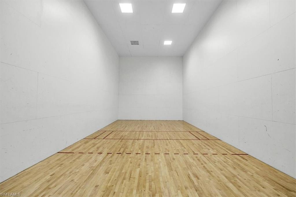 Indoor court featuring wood-finish flooring with court markings, white walls, and integrated ceiling lighting