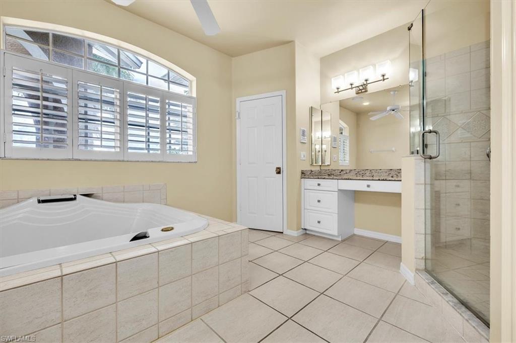 Tiled bathroom featuring a soaking tub, glass-enclosed shower, dual vanity with undermount sinks, and a ceiling fan