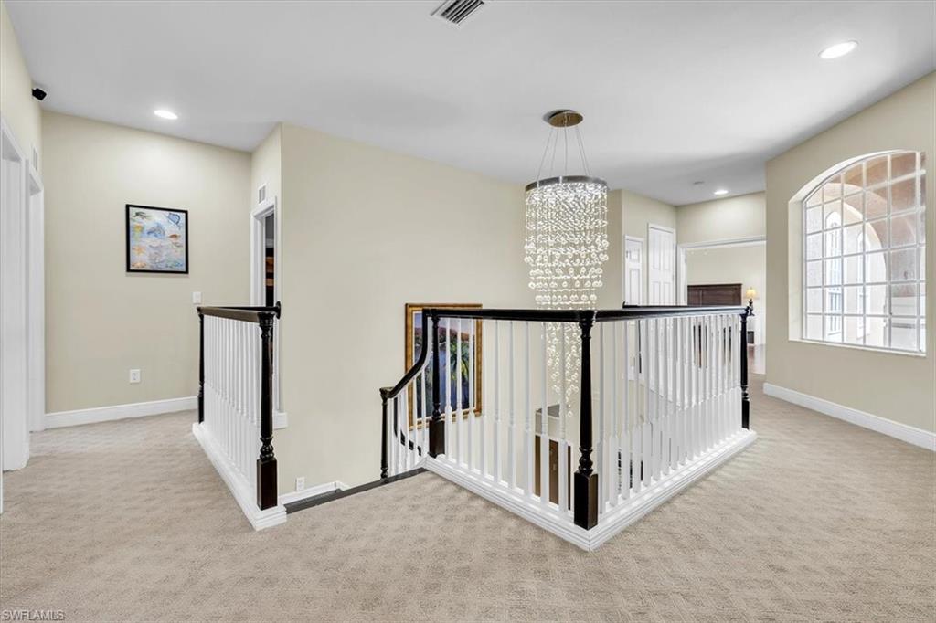 Carpeted hallway featuring a decorative chandelier, white baluster railing with dark wood newel posts, arched glass block window, and recessed lighting