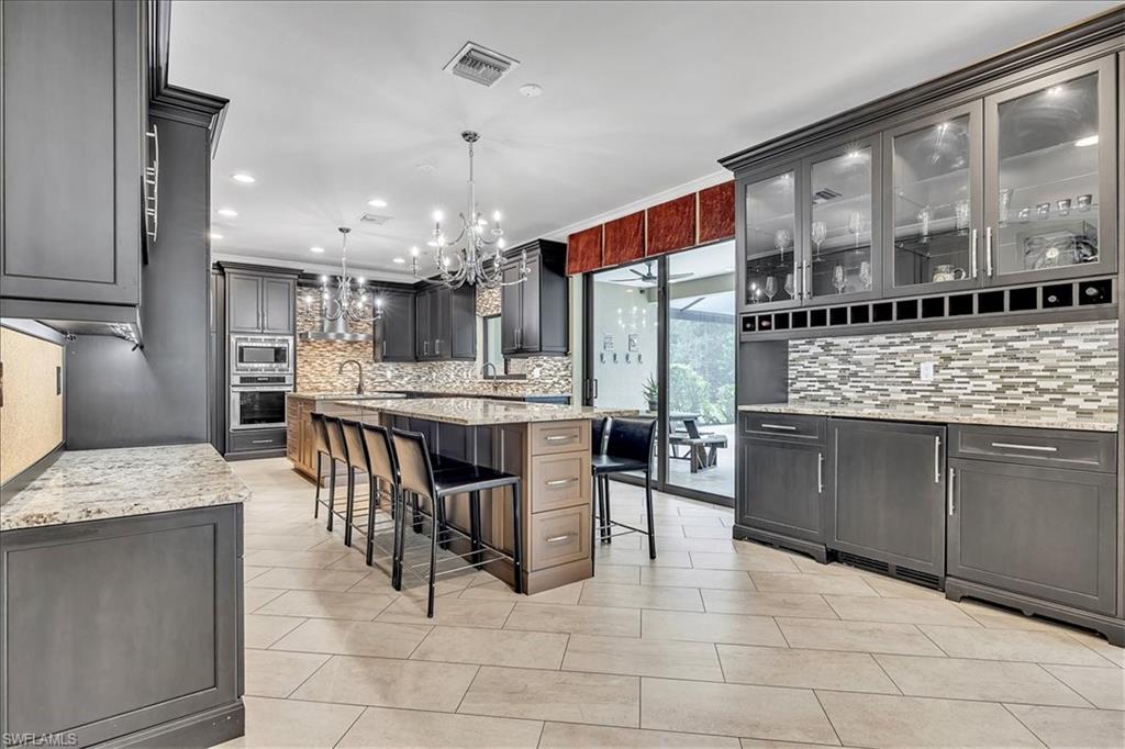 Spacious kitchen featuring dark cabinetry, a large center island with seating, integrated stainless steel appliances, and tile flooring