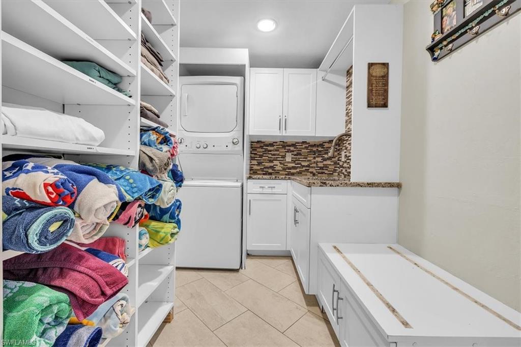 Dedicated laundry area featuring a stacked washer and dryer, white cabinetry, a granite-finish countertop, and a tiled backsplash