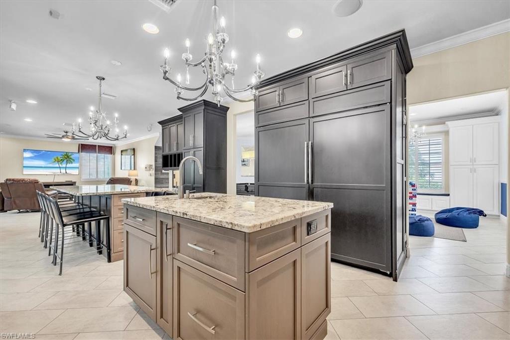 Gourmet kitchen featuring a central island with integrated sink, stone-finish countertops, panel-front refrigerator, and recessed lighting