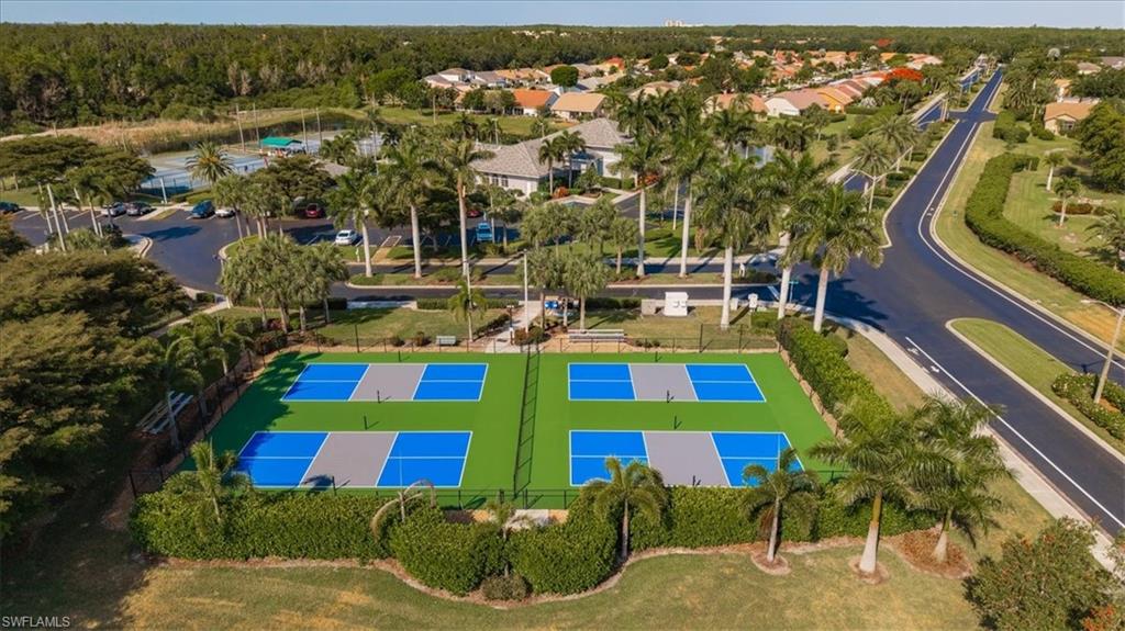 Four vibrant pickleball courts with perimeter fencing, surrounded by lush landscaping and mature palm trees