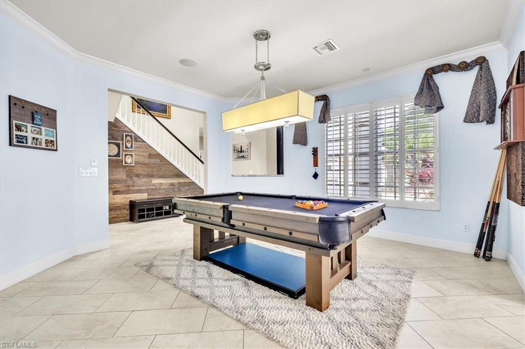 Spacious interior featuring large format tile flooring, crown molding, and a prominent staircase with a wood-panel accent wall