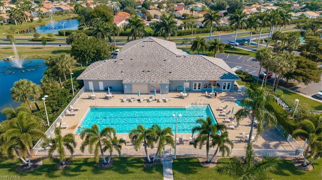 Community clubhouse with a large outdoor swimming pool, paved sundeck, and surrounding palm trees
