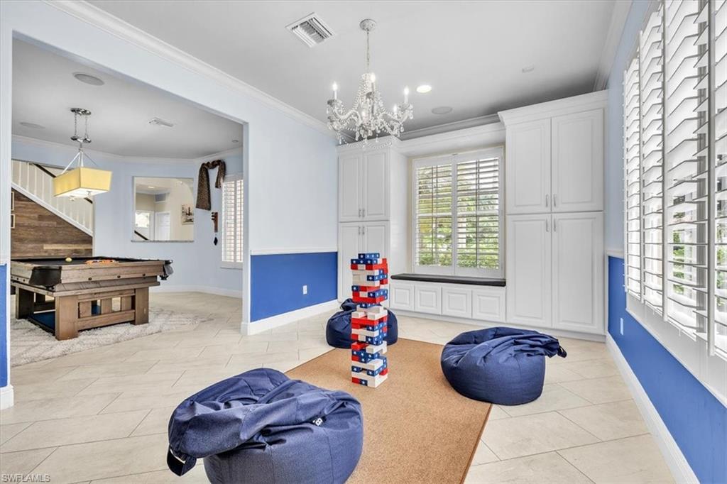 Spacious recreational room featuring light-colored tile flooring, white crown molding, and built-in white cabinetry