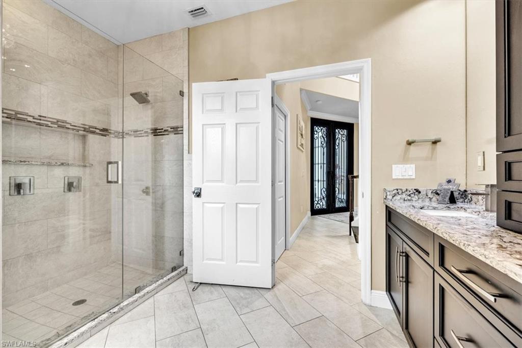 Glass-enclosed shower with tile surround and integrated shelving, dark wood-finish vanity with stone countertop and undermount sink, and light-toned tile flooring