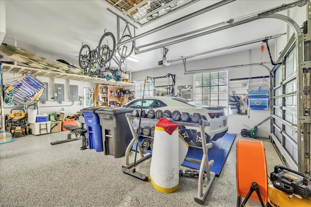 Spacious garage featuring a durable epoxy floor, overhead storage racks, a wall-mounted shelving unit, dual windows with blinds, and exposed garage door mechanisms