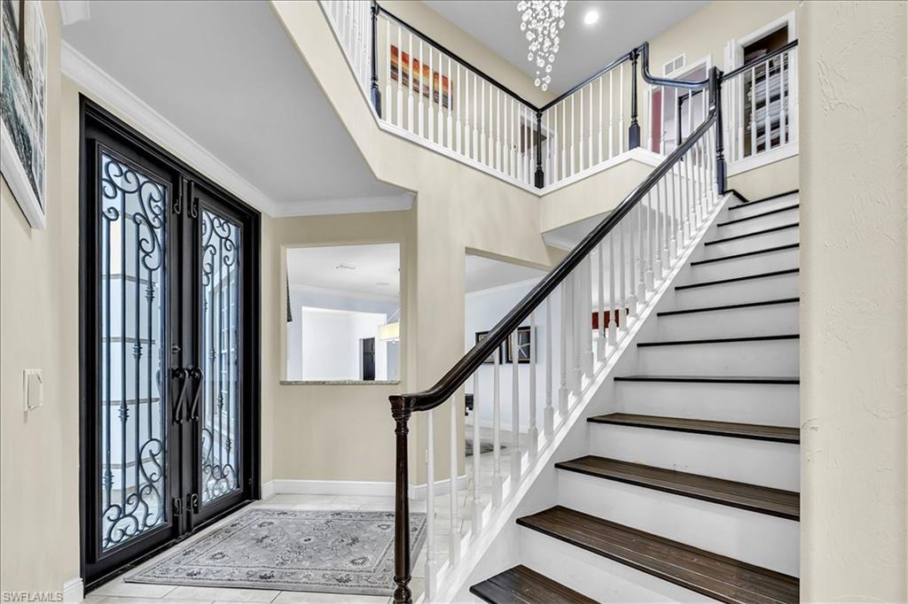 Two-story foyer featuring a double entry door with wrought iron detailing, a grand staircase with dark wood-finish treads and white risers, a second-story landing with matching railings, and a tiered chandelier