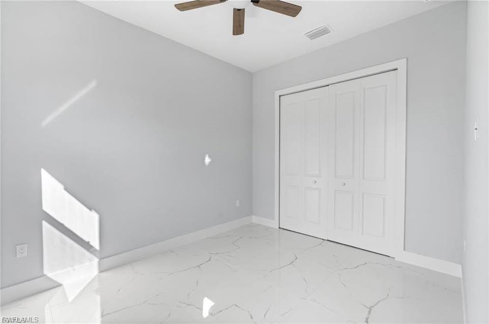 Neutral-toned room featuring a wood-finish ceiling fan, white bi-fold closet doors, and large-format white tile flooring with veining