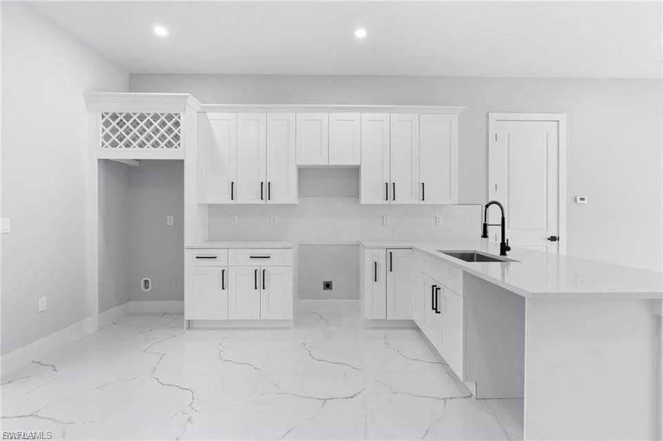 Contemporary kitchen featuring white shaker cabinetry, quartz countertops, a matte black faucet, and large format tile flooring with distinctive veining