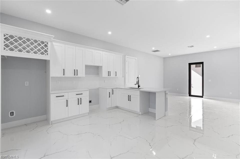 Open-concept kitchen featuring white shaker cabinetry, an island with a built-in sink and matte black faucet, and white countertops