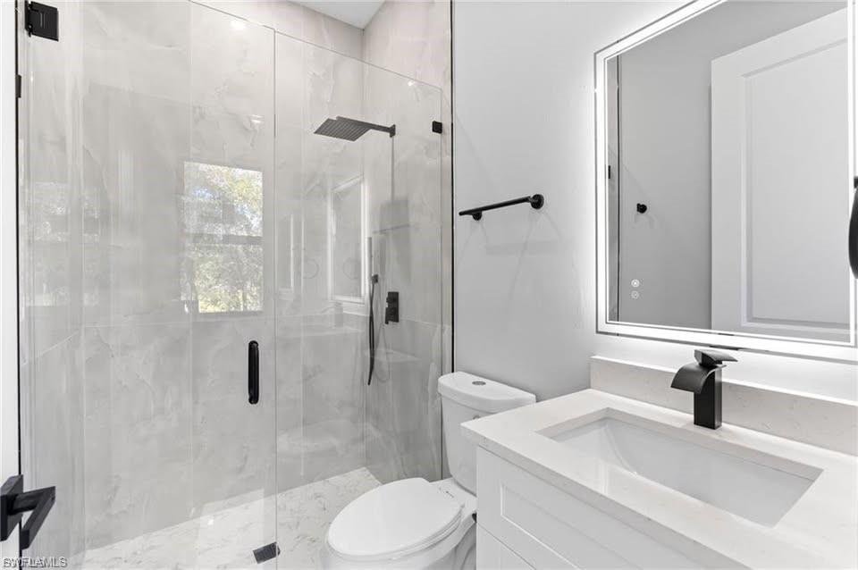 Contemporary bathroom featuring a frameless glass shower enclosure with a rainfall showerhead, large format tiled walls, and a white vanity with an integrated sink, quartz-finish countertop, and matte black faucet