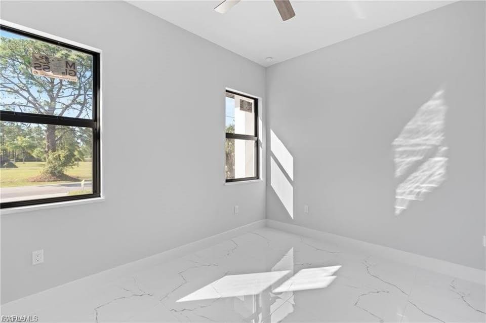 Room featuring two windows with black frames, a ceiling fan, light gray wall paint, and white tile flooring with a subtle veining pattern