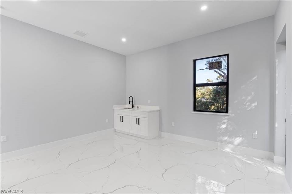 Spacious room featuring white large-format tile flooring, a built-in wet bar with a white cabinet and black faucet, and a black-framed window