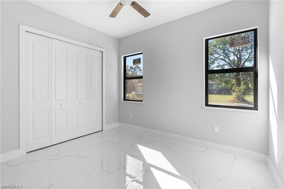 Spacious room featuring large windows, a ceiling fan, bifold closet doors, and marble-look tile flooring