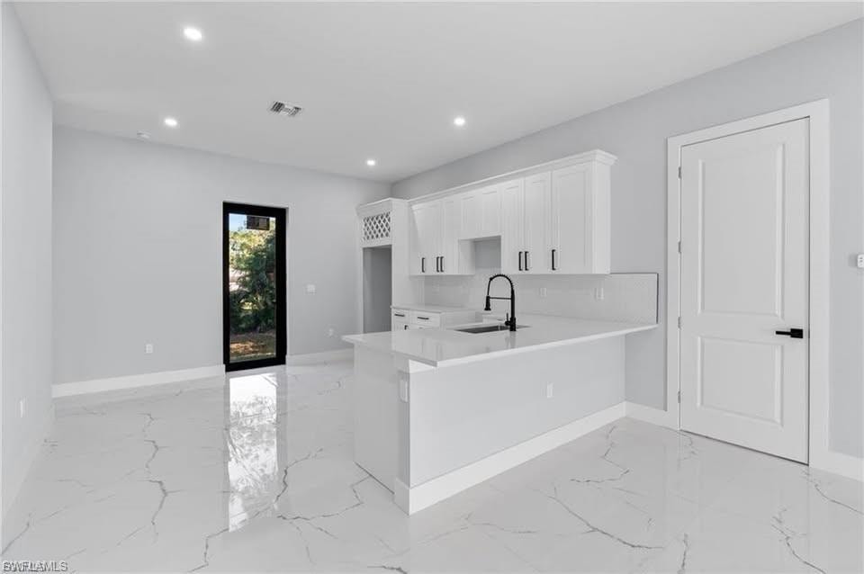 Modern kitchen featuring a white island with an integrated sink and matte black faucet, white shaker cabinetry with matte black hardware, and an adjacent pantry door