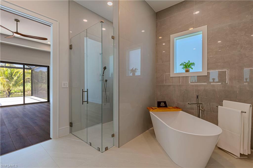 Contemporary bathroom featuring a freestanding soaking tub with floor-mounted faucet, a glass-enclosed shower, and large format wall tiling