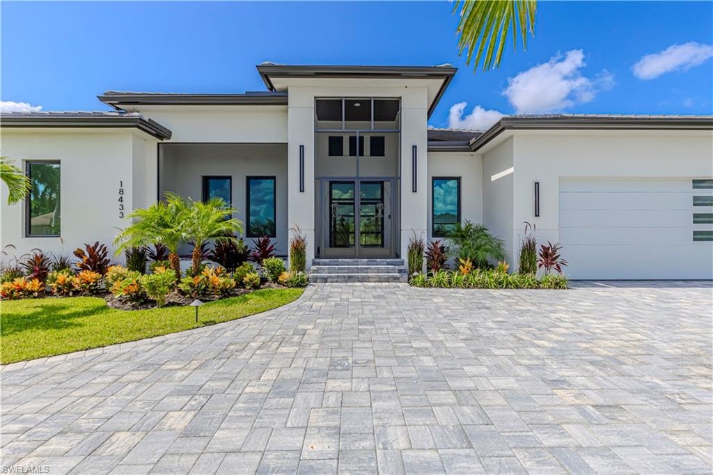 Modern architectural facade featuring a prominent double-door entry with transom windows, a paver driveway, and an integrated garage