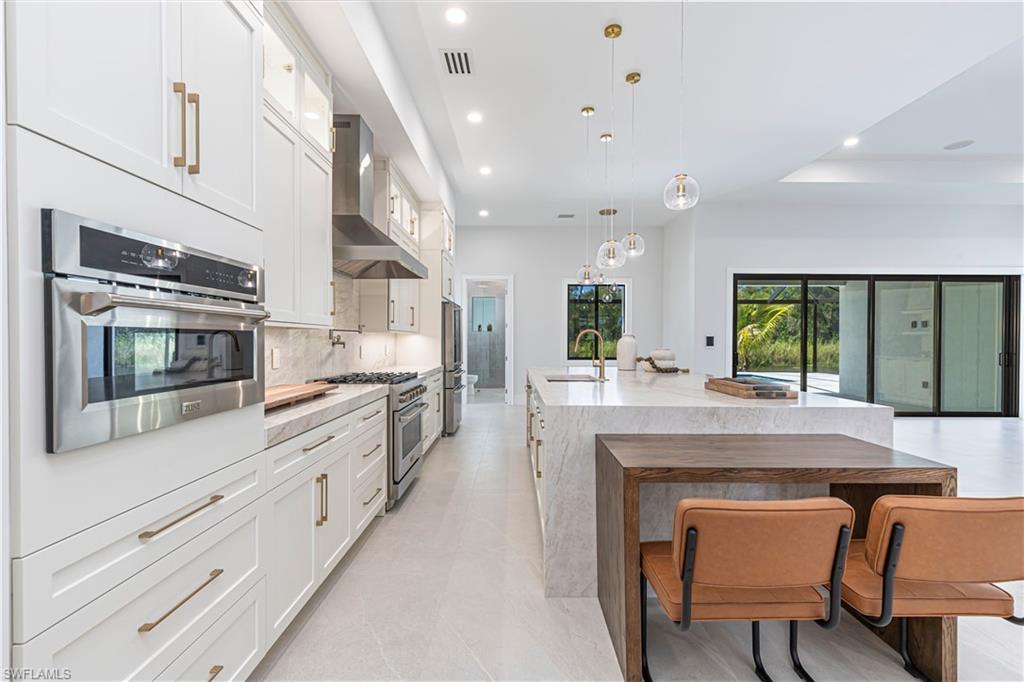 Modern kitchen featuring white shaker cabinetry, stainless steel appliances, a large center island with an integrated dining surface, and sleek pendant lighting