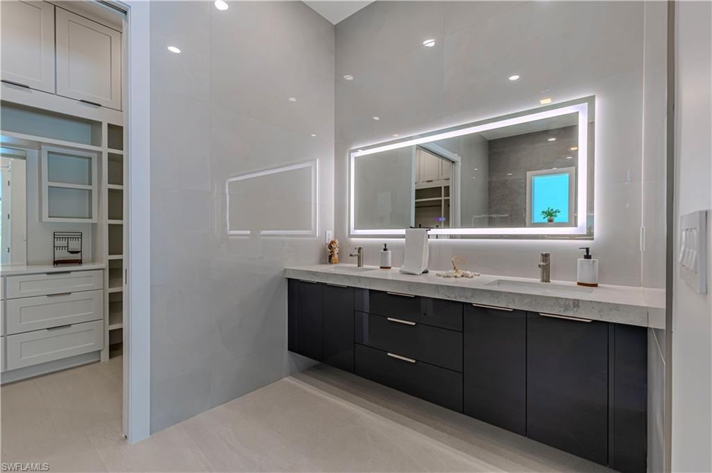 Double vanity with integrated sinks, a floating dark wood-finish cabinet, and a large backlit mirror