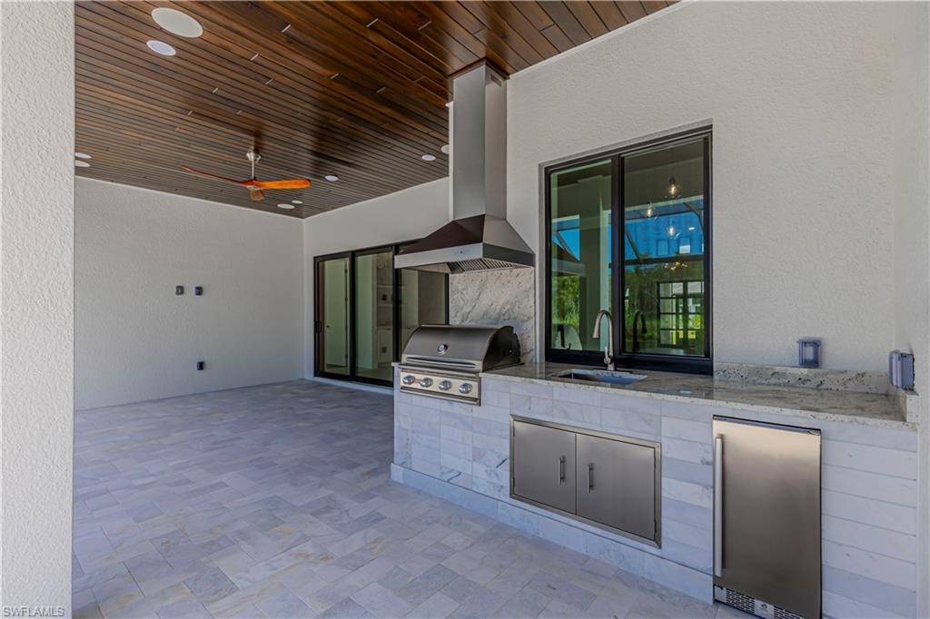 Outdoor kitchen with built-in grill, stainless steel hood, sink, and undercounter refrigerator