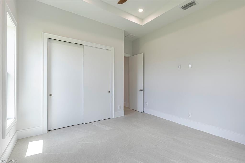 Spacious room featuring light gray carpeting, crisp white walls, and a recessed tray ceiling