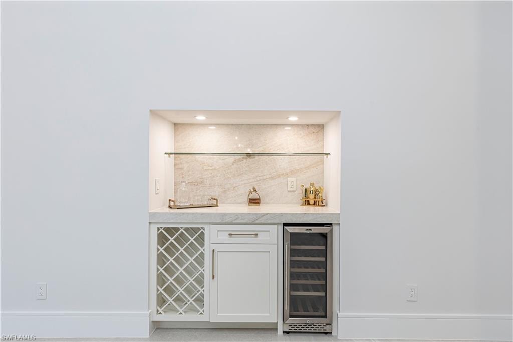 Built-in wet bar with white cabinetry, stone countertop, integrated wine rack, and beverage refrigerator