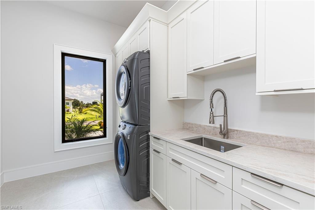 Laundry area featuring stacked appliances, ample white cabinetry, a utility sink with a high-arc faucet, and light-toned countertops