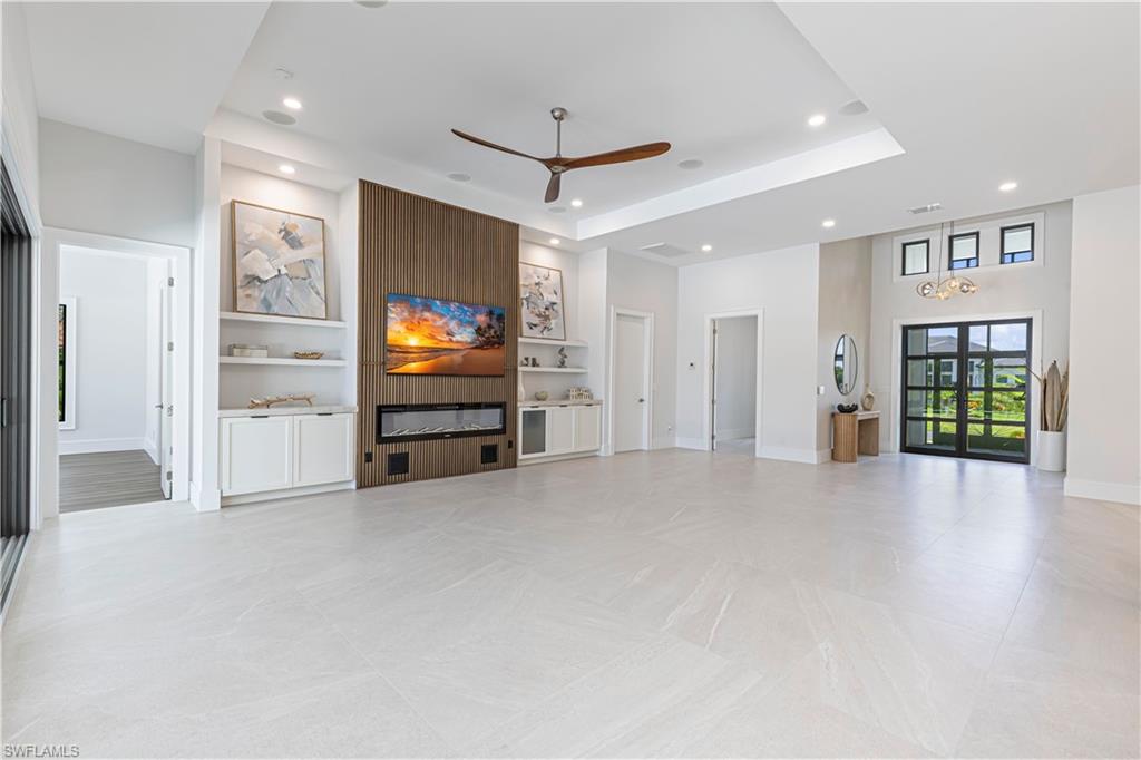 Spacious living area featuring light-toned tile flooring, recessed lighting, and a wood-paneled accent wall with a built-in electric fireplace
