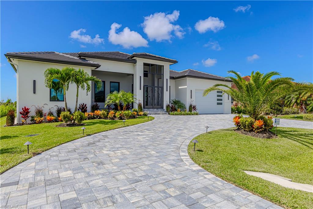 Modern stucco exterior with a dark tile roof, an expansive paver driveway, and a two-car garage