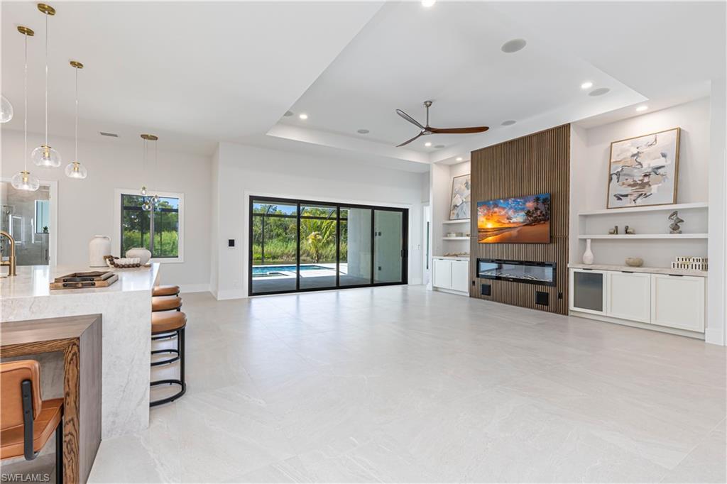 Spacious room featuring light-toned tile flooring, a wood-paneled accent wall with an integrated electric fireplace, and built-in white cabinetry with open shelving