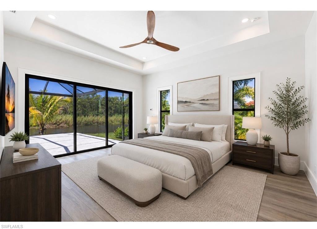 Virtual Staged. Spacious room featuring large sliding glass doors opening to an outdoor patio with a water feature, tray ceiling with a ceiling fan, recessed lighting, and wood-finish flooring