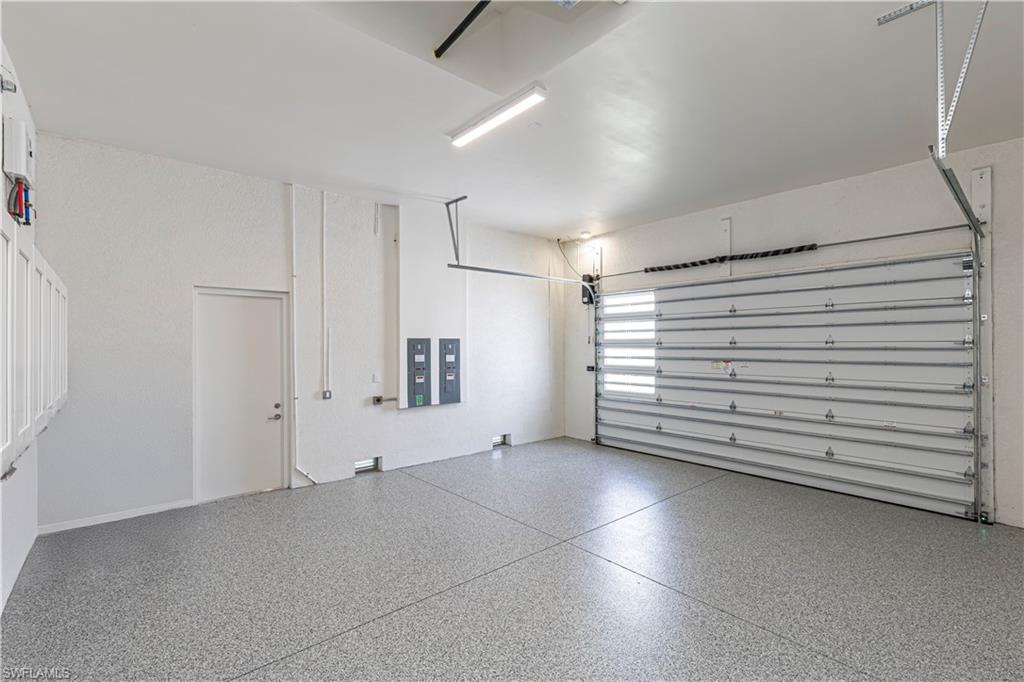Spacious garage featuring an epoxy-coated flooring, white shaker-style cabinetry, and a roll-up garage door with frosted window panels