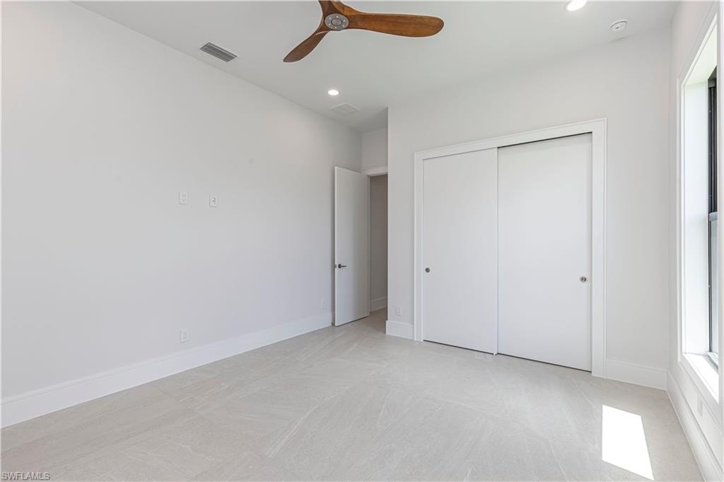 Spacious interior room featuring light-toned flooring, bright white walls, and a wood-finish ceiling fan