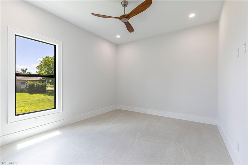 Well-lit room featuring light-toned flooring, a single window with white trim, recessed lighting, and a ceiling fan with wooden blades