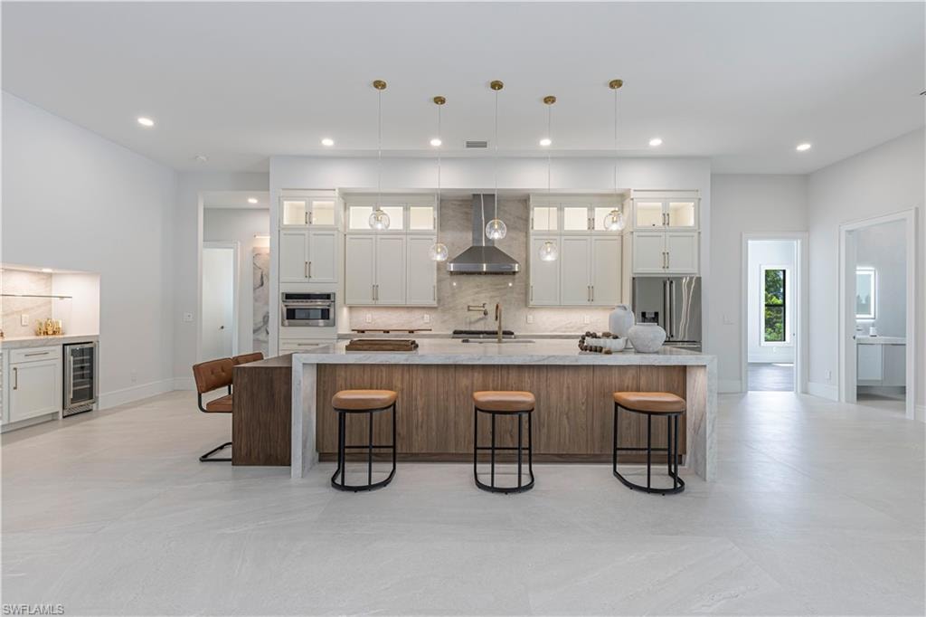 Gourmet kitchen featuring a large central island with seating, stainless steel appliances, white cabinetry with glass inserts, and a built-in beverage refrigerator