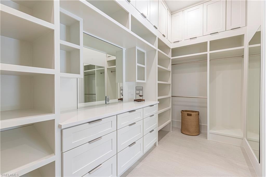 Custom closet system featuring white cabinetry and shelving, integrated mirrors, built-in drawers with modern hardware, hanging rods, and light-toned flooring