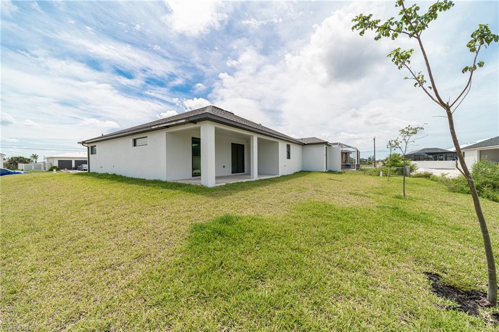 Spacious rear yard with covered lanai, white exterior finish, dark roof, and multiple windows
