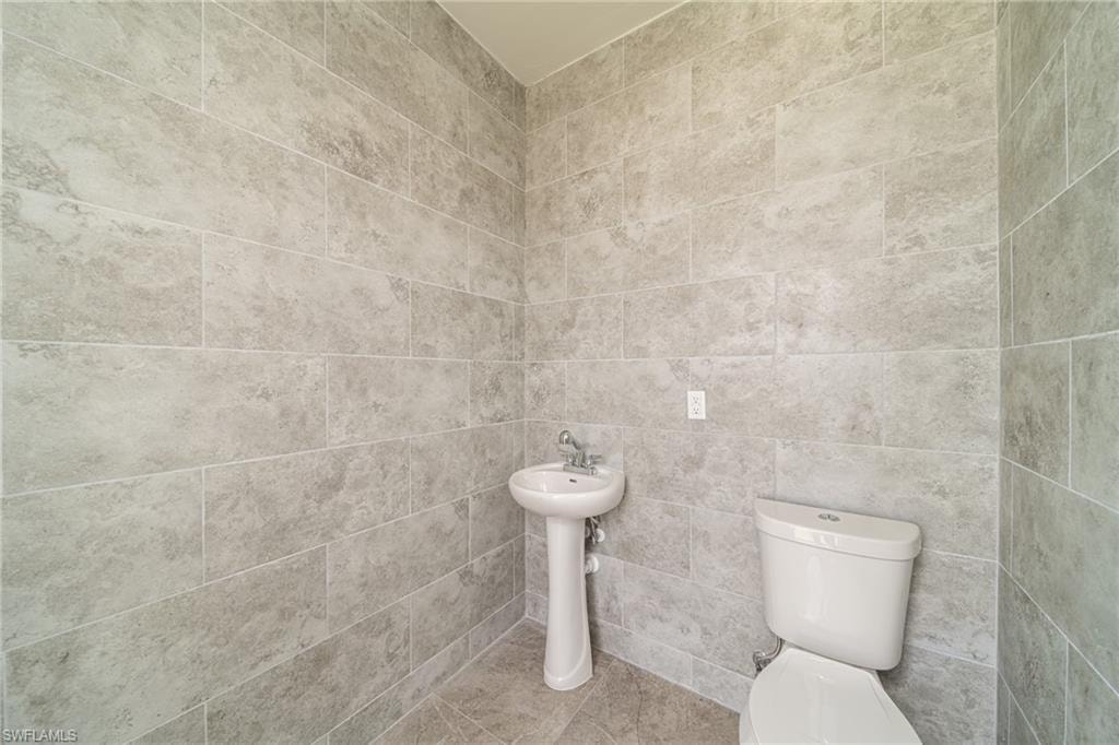 Bathroom featuring large format wall tiling, matching floor tiles, a pedestal sink with chrome fixtures, and a white toilet
