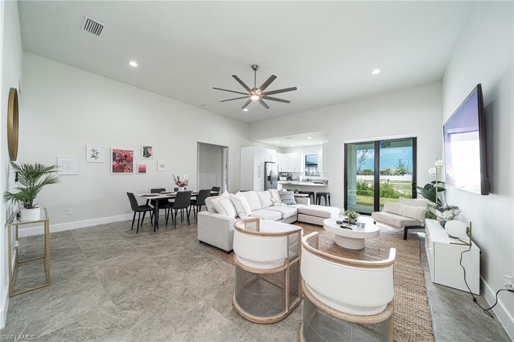 Open-concept living space featuring high ceilings, gray large-format tile flooring, a contemporary ceiling fan, and sliding glass doors leading to the exterior