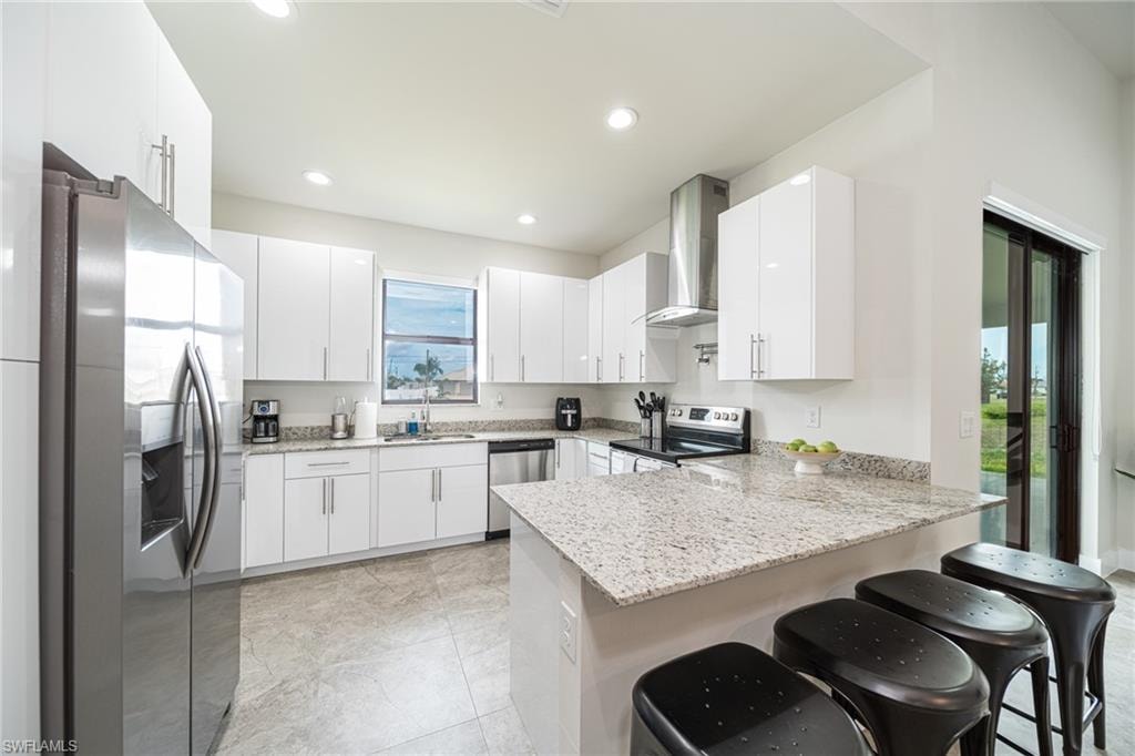 Modern kitchen featuring white cabinetry, stainless steel appliances, a granite countertop island, recessed lighting, and tile flooring