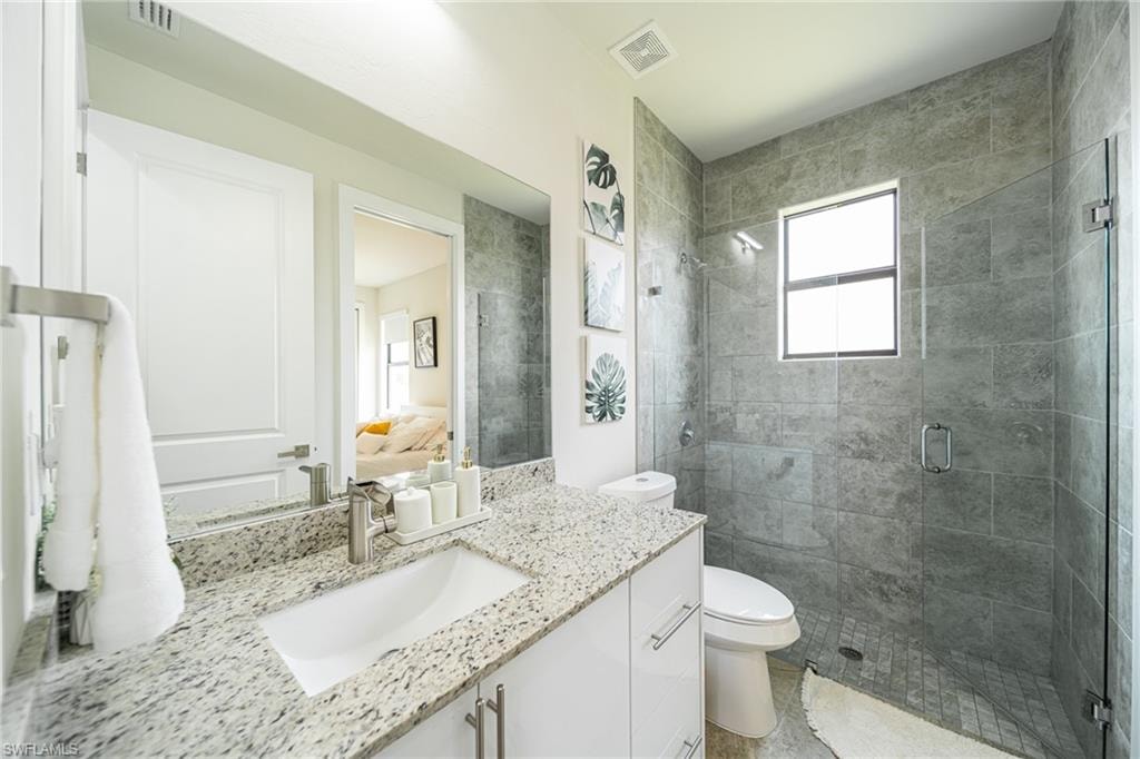 Bathroom featuring a granite countertop vanity with an undermount sink, a large wall mirror, a floor-to-ceiling tiled shower with a glass enclosure, and a frosted window