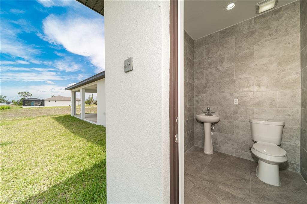 Powder room featuring neutral-toned wall and floor tile, a pedestal sink with chrome faucet, a white toilet, and recessed lighting