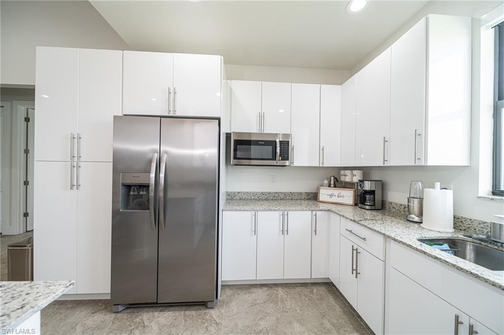 Modern kitchen featuring extensive white cabinetry, stainless steel appliances, speckled stone countertops, and tile flooring