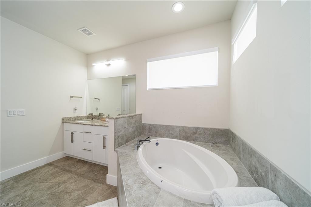 Soaking tub with surrounding stone-finish tile and a dual vanity with granite countertop